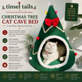 A fluffy white cat sits inside a green Christmas tree-shaped cat cave bed with a red bow